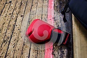 Red boxing glove on the gym floor with wooden covering. Nearby is a black backpack. Sports and training, wrestling and endurance,