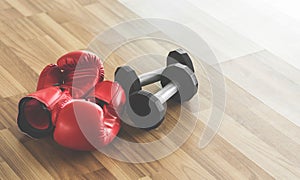 Red boxing gloves with dumbbells on wooden floor.