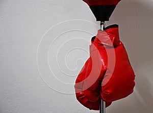 Red boxing gloves hanging on punching ball pole on concrete wall