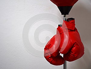 Red boxing gloves hanging on punching ball pole on concrete wall