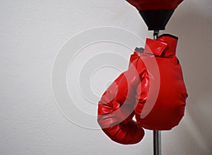 Red boxing gloves hanging on punching ball pole on concrete wall