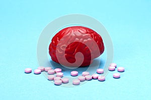 Red brain on a blue background with pink pills. Some pills for the brain. It is symbolic for drugs