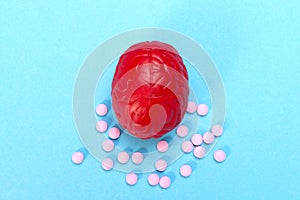 Red brain on a blue background with pink pills. Some pills for the brain. It is symbolic for drugs