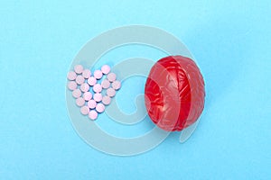 Red brain on a blue background with pink pills. Some pills for the brain. It is symbolic for drugs