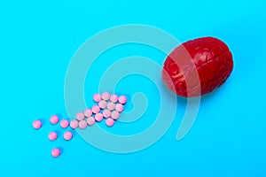 Red brain on a blue background with pink pills. Some pills for the brain. This is symbolic for drugs, psychopharmaceuticals,