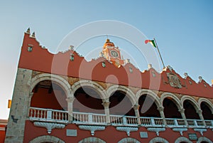 Red brick building tower with golden dome and clock in the City center of Merida. Mexican flag flutters on air. City Town hall of