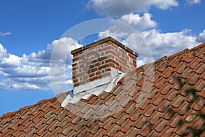 Red brick chimney designed on slate roof of house building outside against blue sky with white clouds background