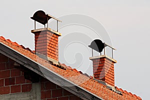 Red brick chimneys with metal protection on top on unfinished suburban family house at sunset