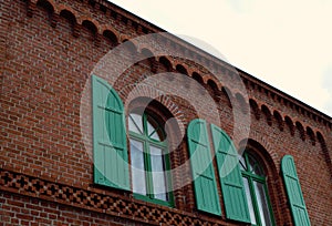 Red brick facade with two windows with green shutters