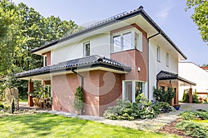 Red brick house with terrace and green grass and trees during summer