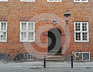 Red brick wall, black door, white windows, old lantern and two bicycles parked near the threshold