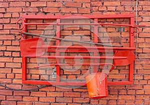 Red brick wall with a red paint bucket and a shovel in the foreground