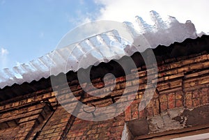 Red brick wall, roof with melting ice falling, view from ground on blue cloudy sky