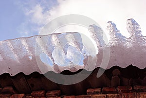 Red brick wall, roof with melting ice falling, view from ground on blue cloudy sky background close up