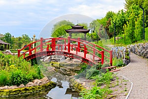 Red bridge and gazebo by pond in Japanese garden