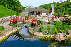 Red bridge and gazebo by pond in Japanese garden