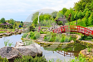 Red bridge and gazebo by pond in Japanese garden