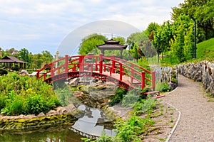 Red bridge and gazebo by pond in Japanese garden