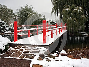 Red bridge and snow falling in Japanese garden photo