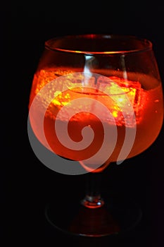 Red bright glowing ice cubes that float in a delicious frosted white cold drink are located in a cognac glass on a black frosted b