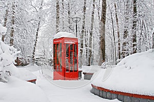 Red British telephone booth used as street library in winter