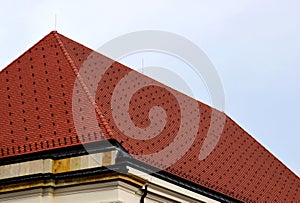 Red and brown steep clay tile roof. steep slope. Zink roof edge flashing. pale sky