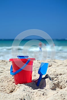 Red bucket and blue spade on sunny sandy beach