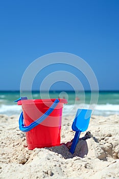 Red bucket and blue spade on sunny, sandy beach