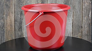 Red bucket isolated on black and wooden background. Side view. Loop motion. Rotation 360.