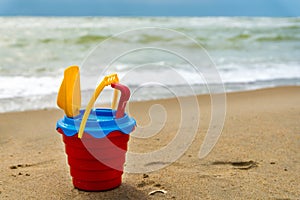 Red bucket with a shovel, a rake and a net on the beach