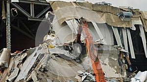 Red building machine dismantles rubble of ruined sport arena