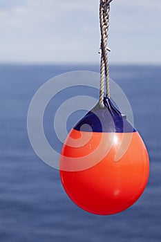 Red buoy hanging in rope by ship with the sea in the background