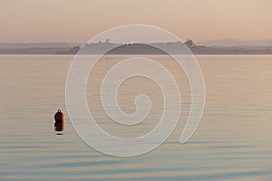 A red buoy on Trasimeno lake at sunset, with Castiglione del Lag