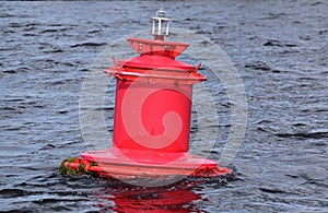 Red buoy on the undulating surface of the river. Lantern at the top of the buoy