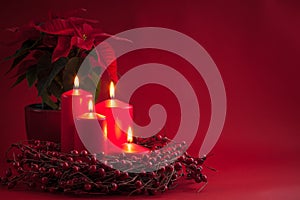 Red burning Advent Christmas candles with the berries wreath and poinsettia on a red background