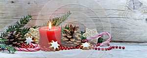 Red burning candle and Christmas decoration on cold gray wooden planks, panoramic banner format, copy space