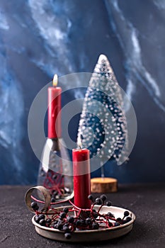 Red burning candle in rustic holder, wid blue berries and blue decorative tree