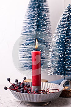 Red burning candle in rustic holder, wid blue berries and blue decorative trees