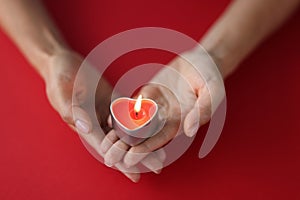 Red burning candle in the shape of a heart in female hands on red background