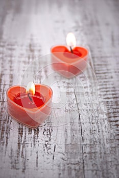 Red burning heart shaped candles on rustic white wooden table