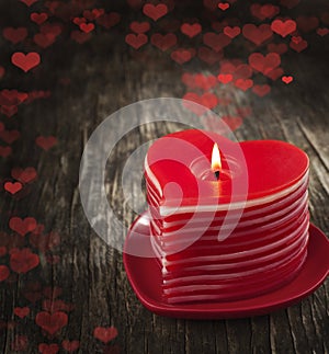 Red burning heart shaped candles on wooden background.