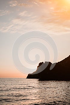 A red burning sunset over the sea with rocky volcanic cliff. Abstract nature summer or spring ocean sea background.