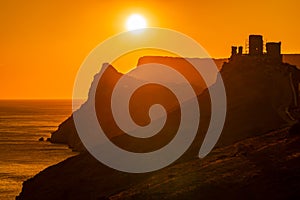 A red burning sunset with the silhouett of a cliff and castle over the sea