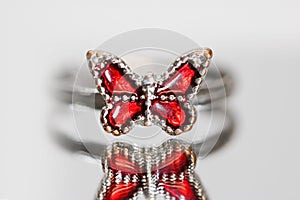 Red butterfly finger ring with reflection on grey background