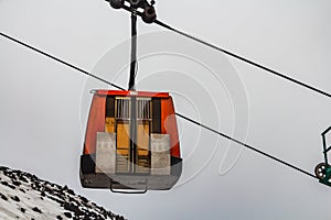 A red cabin of the cable cars with closed door under the black vulcan mountain Etna with white snow on the gray sky background in