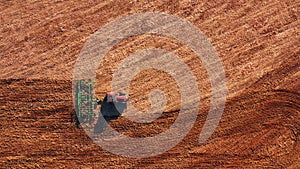 Red cabin tractor plowing the field with green plough, aerial view.