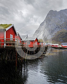 Red cabins perched atop a dock on a tranquil lake surrounded by lush mountains.