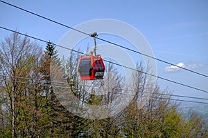 Red cable car cabin against trees and blue sky