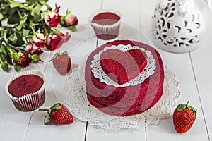 Red cake without cream `red velvet` on a white wooden table, decorated with strawberries, roses and white openwork vase with a hea