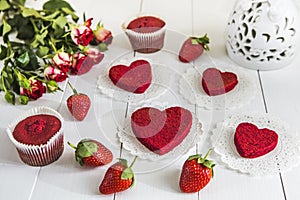 Red cake without cream `red velvet` on a white wooden table, decorated with strawberries, roses and white openwork vase with a hea